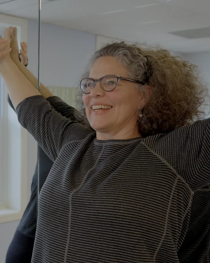 Client smiling during an assisted overhead arm raise with her posture therapist