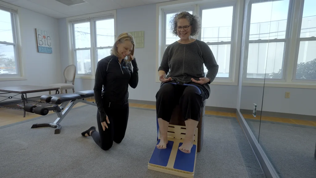 Posture therapist kneeling beside a client seated on an alignment platform during a session