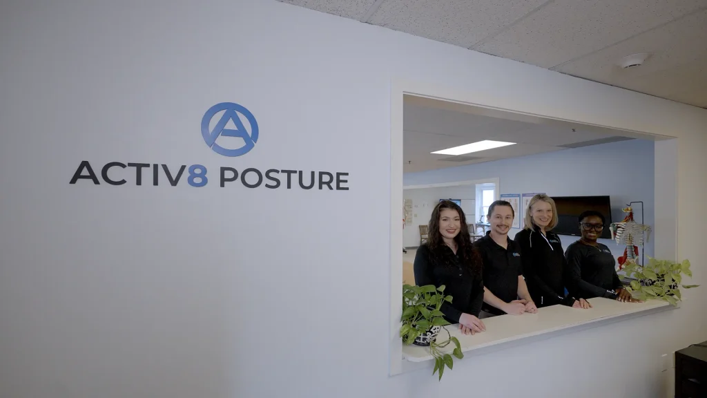 The Activ8 Posture team at the clinic reception desk beneath the Activ8 Posture sign